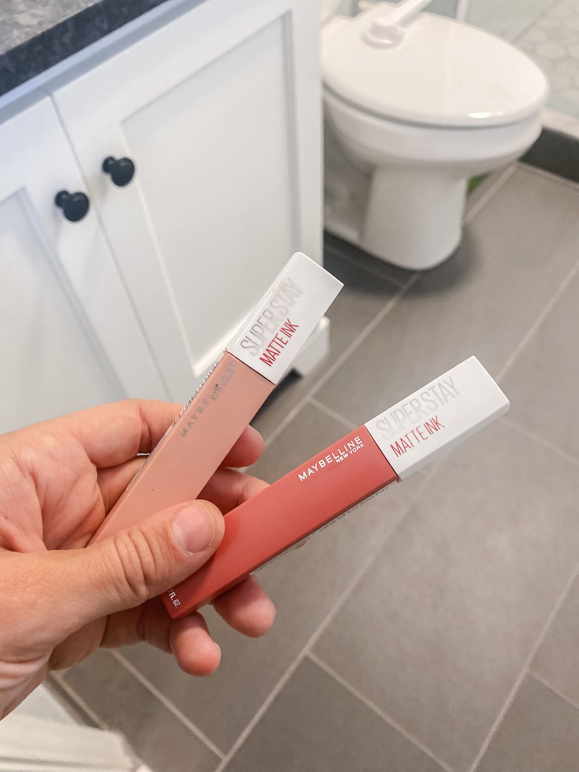 hand holding maybelline lipstick in bathroom